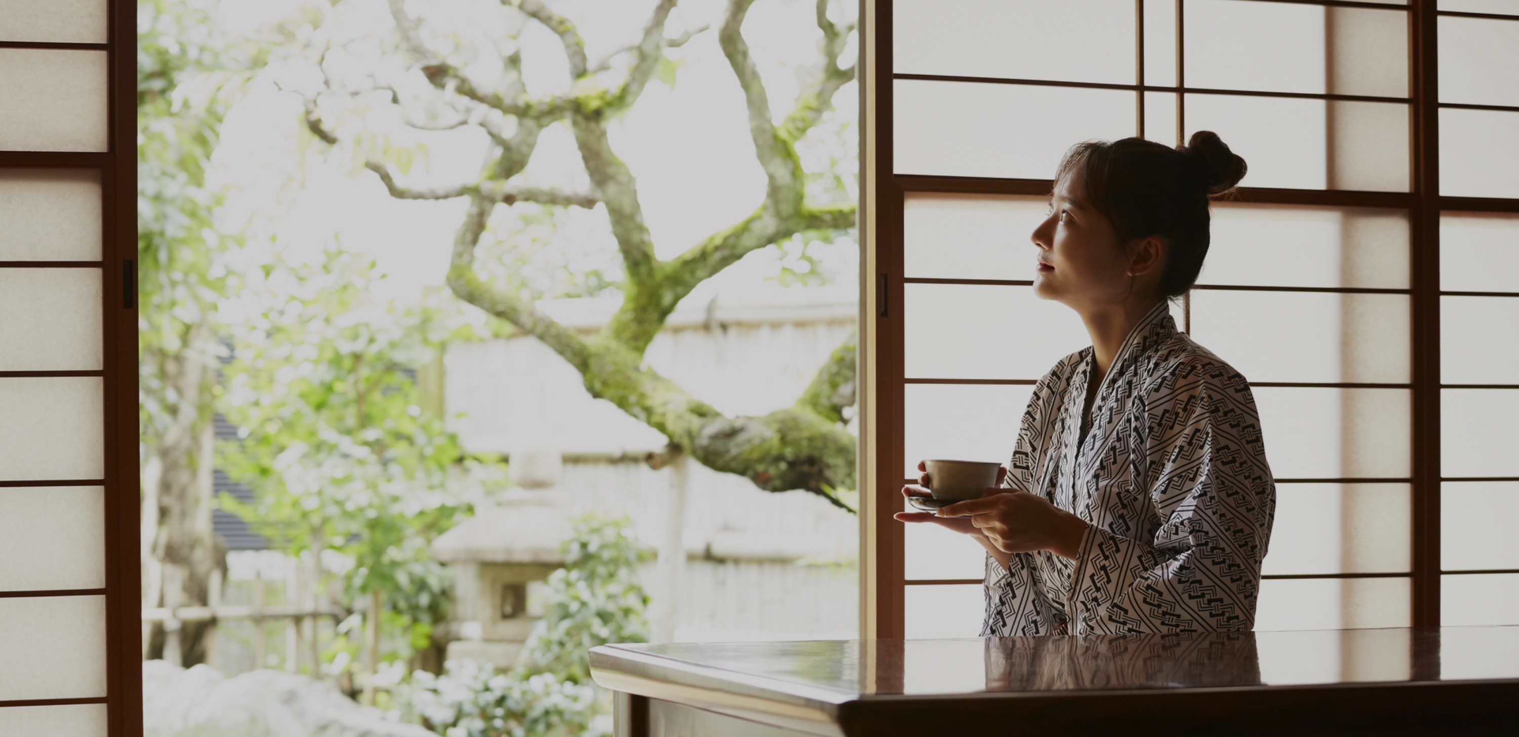 窓の近くで外を見ている着物姿の女性